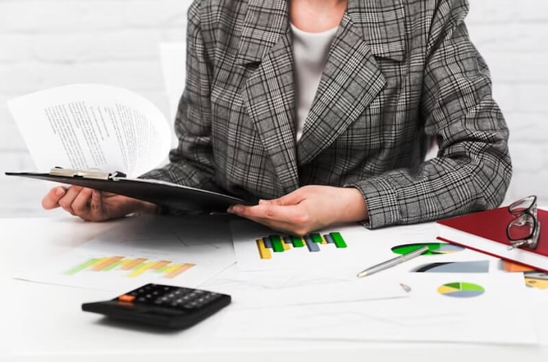 person hand holding paperboard and calculator, papers and book on a table