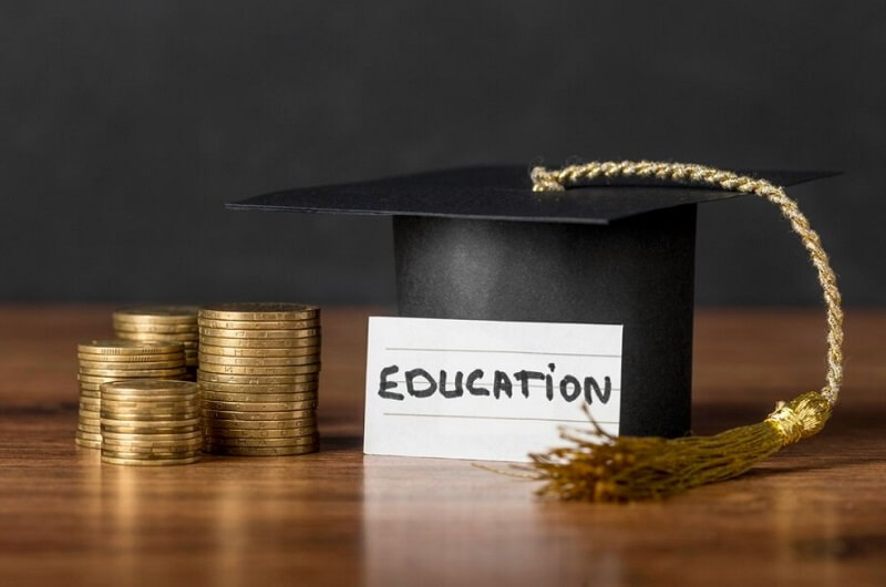 graduation cap and some coins with paper on a wooden table